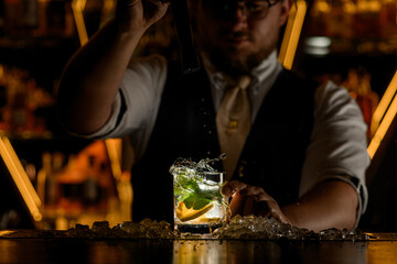 The bartender jerked the portable mixer out of the cocktail with lemon wedges and mint leaves, so that the drops flew onto the bar