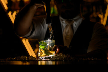 Bartender sharply pulls portable mixer out of cocktail with lemon wedges and mint leaves