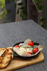 Grilled Camembert cheese with tomatoes and toasted bread. Camembert in a grill pan on a wooden board.