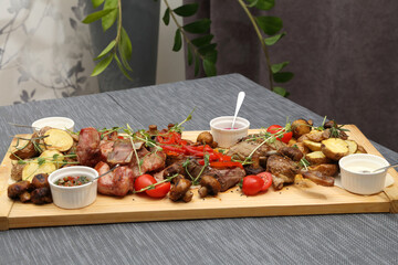 A large wooden board with appetizers: duck, steaks, mushrooms, tomatoes and various sauces for four people. A huge wooden board with excellent meat and vegetable appetizers.