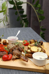 A large wooden board with appetizers: duck, steaks, mushrooms, tomatoes and various sauces for four people. A huge wooden board with excellent meat and vegetable appetizers.