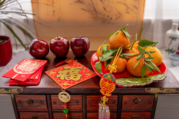 A plate of tangerines and red apples. Red packets and Chinese New Year decorations with good luck, wealth and fortune words. A Chinese New Year background, concept.