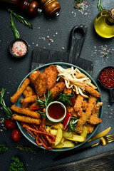 Fast food. Plate with snacks: nuggets, sausages, French fries, cheese sticks. On a black stone background. Free space for text.