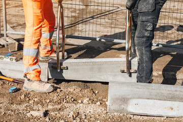 Construction workers align concrete kerb blocks on a building site during daylight hours