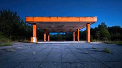 An abandoned gas station at dusk features an orange canopy on cracked concrete, overgrown with weeds. Lush greenery surrounds the site, contrasting with the serene twilight sky.