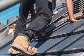 A worker carefully installs roofing tiles on a sunny day at a construction site, ensuring quality and safety on the sloped surface