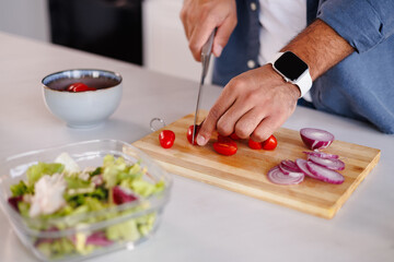 Close up of african american man cutting cherry tomatoes for fresh salad in kitchen
