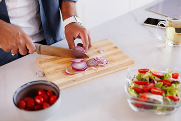Partial shot of african american man cutting onion near fresh salad, tea and smartphone in kitchen