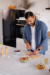 Cheerful african american man cutting onion while cooking near tea in kitchen