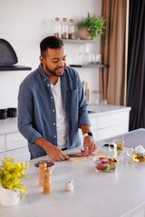 Joyful african american man taking sliced onion while cooking fresh salad near tea in kitchen