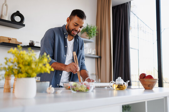 Positive african american man cooking near fresh salad and herbal tea in kitchen
