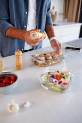 Partial view of african american man adding spices to raw chicken legs in baking form near fresh salad in kitchen
