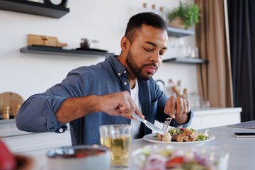 African american man eating tasty meal near fresh salad and herbal tea at home