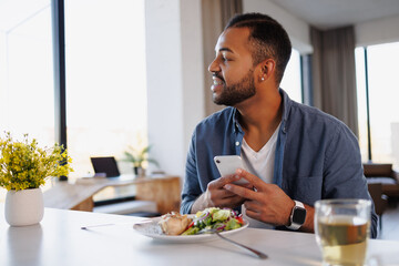 Smiling african american man using smartphone near delicious lunch and tea at home