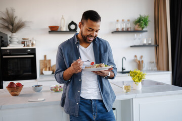 Smiling african american man holding salad and chicken legs on plate in kitchen