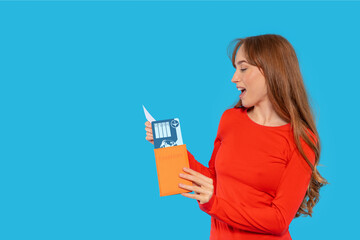 Young woman excitedly opens an envelope revealing travel documents against a bright blue background