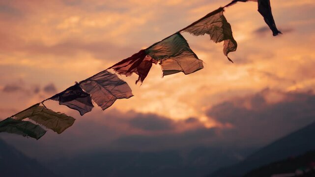 4K Rack focus shot of prayer flags waving in the wind in front of snowy Himalayan mountain peaks covered by clouds during the sunset at Khangsar village in Lahaul valley, Himachal Pradesh, India.