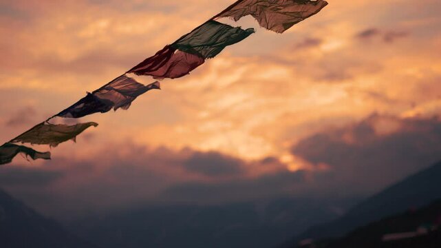 4K Slow motion shot of prayer flags waving in the wind in front of snowy Himalayan mountain peaks covered by clouds during the sunset at Khangsar village in Lahaul valley, Himachal Pradesh, India.	