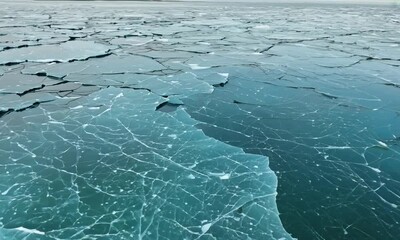 Frozen Water Abstract:  A captivating aerial view of a frozen lake or ocean, showcasing intricate patterns of cracked ice and shimmering turquoise water. - Powered by Adobe
