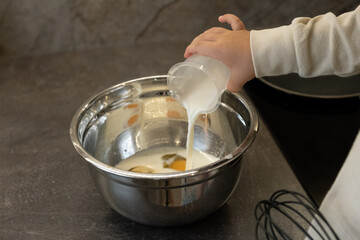 A small hand holds a measuring cup and pours milk into a bowl