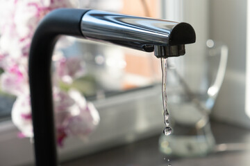 Water flows from a black tap in a kitchen with a window