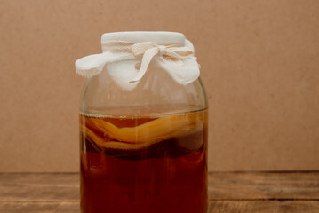 A glass jar with a beige kombucha drink is covered with a textile lid and tied with a ribbon. Close-up with space for text