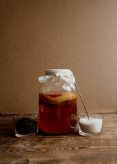 A glass jar with a kombucha drink on a wooden background and ingredients for the preparation of the drink, sugar and tea in glass bowls. Preparation of homemade healthy drink with probiotic