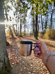 Close-up of female hand holding cup tea on background forest and sky during warm sunrise or sunset