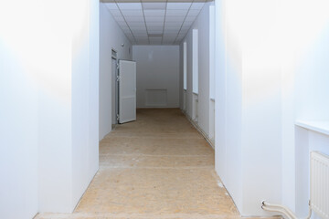 Long corridor in an old school with worn flooring and faded walls, awaiting renovation