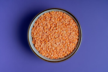 Raw red lentils, high in protein, in a bowl on blue background