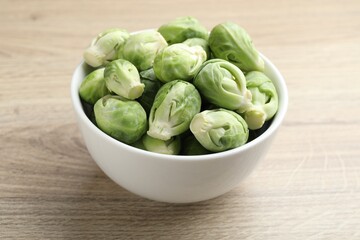 Fresh green Brussels sprouts in bowl on wooden table, closeup