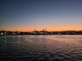 Naklejka premium evocative image of the sun setting behind the sea coast with the solhoutte of the port in the background in Italy