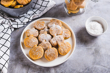 Homemade pumpkin shaped cookies in powdered sugar on a plate on a table