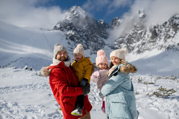 Naklejka premium Young family is enjoying winter holiday in the mountains, standing in the middle of snowy landscape.