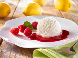  Zitronensorbet mit Himbeeren und Himbeersauce auf weissem Teller auf rustikalem Holzfond mit gruener Serviette, Eiscreme, Zitroneneis, sorbet, 