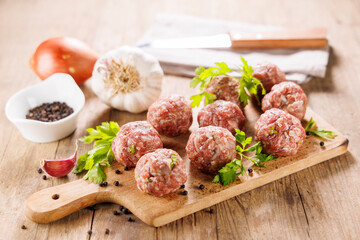 raw meatballs on wooden board with herbs