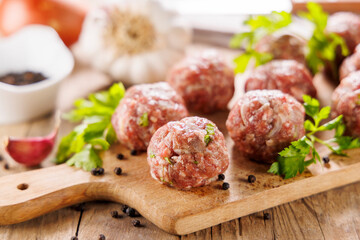 raw meatballs on wooden board with herbs