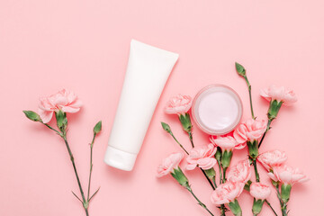 White facial cream tube mockup with cream bottle and pink flower on pink background. Delicate skincare