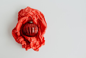 Red vintage Christmas tree ball on crumpled red wrapping paper on white background. Space for text