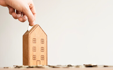hand of someone put coin to house money box with step of growing coins, money saving or investing for home or real estate concept