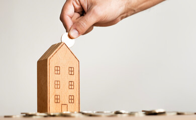 hand of someone put coin to house money box with step of growing coins, money saving or investing...
