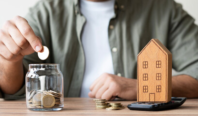 hand of someone put coin to house money box with step of growing coins, money saving or investing for home or real estate concept