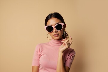 Fototapeta premium Stylish woman in pink outfit and sunglasses posing against beige background