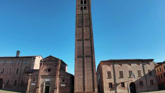 The civic tower of Carpi of church Santa Maria in Castello stands tall in piazza dei martiri, its intricate brickwork shining under a vibrant blue sky, creating a captivating scene in the heart of the