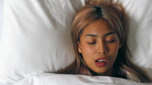 Tired and stressed Asian woman with colored hair sleeping, having bad dream, nightmare with bruxism or grinding teeth
