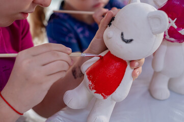 A cute girl with dark hair paints a bearbrick with colorful water paints. Creative studio. Close up