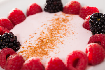 Raspberries and blackberries laid out on a white plate in circle with yogurt and cinnamon