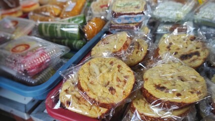 An assortment of traditional Indonesian snacks, with the spotlight on 'kue lumpur,' a soft, sweet cake made with coconut milk and potatoes, packaged and ready to enjoy.