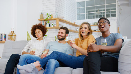 Group Of Friends Sitting On Sofa And Watching Movie At Home Whilst Drinking Wine