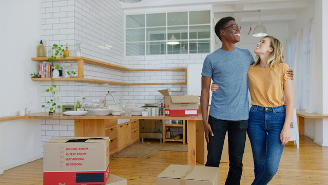 Smiling Young Couple Looking Around Surrounded By Packing Boxes Moving Into New Home - Powered by Adobe